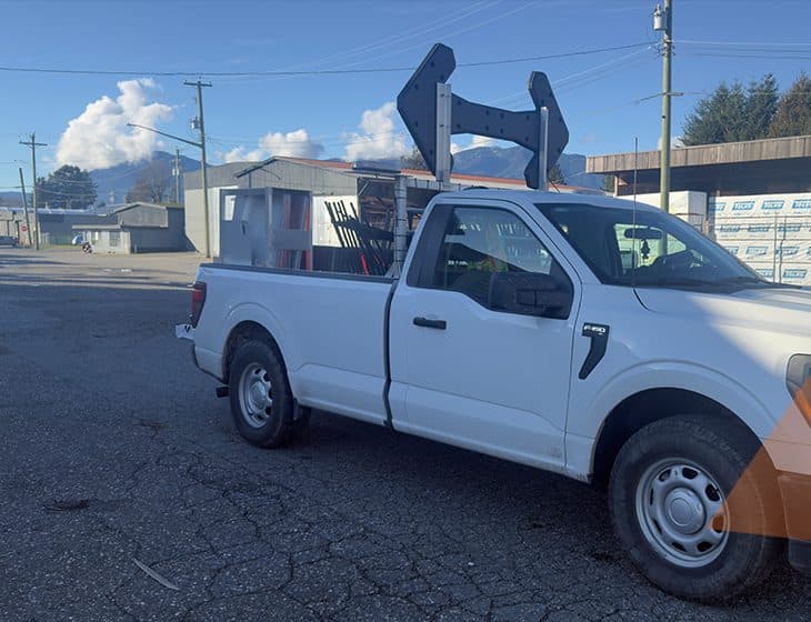 A traffic control truck loaded and staged in a yard, arrow board folded upright above the cab and signage racked in the bed, ready to be dispatched.