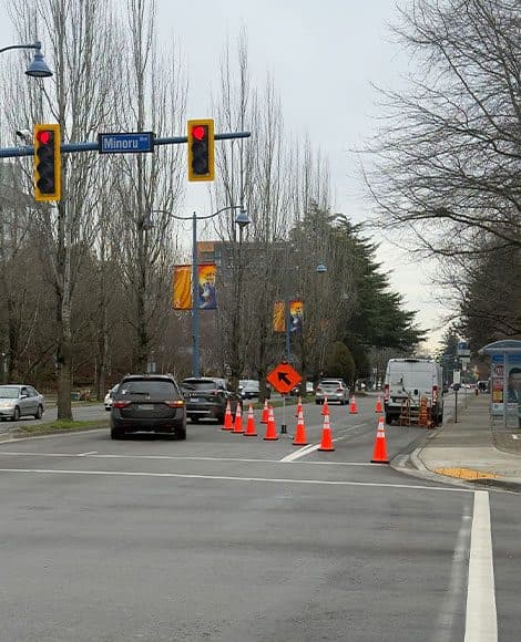 A lane closure on a signalised municipal arterial, with a cone taper, a keep-right sign and a works van occupying the closed lane while traffic passes in the lane alongside.